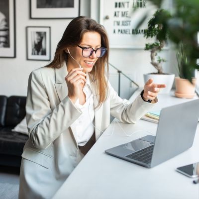 Positive female manager in earphones working on computer, consulting clients online, sitting in cozy coworking space