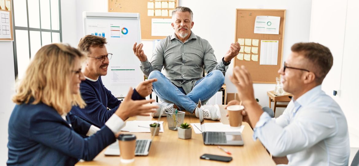 Businessman enjoys meditating during meeting. Sitting on desk near arguing partners at the office.