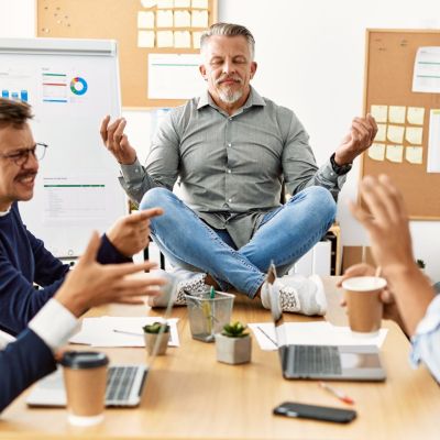 Businessman enjoys meditating during meeting. Sitting on desk near arguing partners at the office.